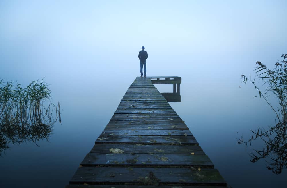 A man stands on a foggy dock, possibly seeking solace and reflection, in line with tips from an anger counselor to tame emotions amidst controversial tweets.