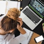 An anxiety ridden woman holds her head in worry while sitting at a desk.