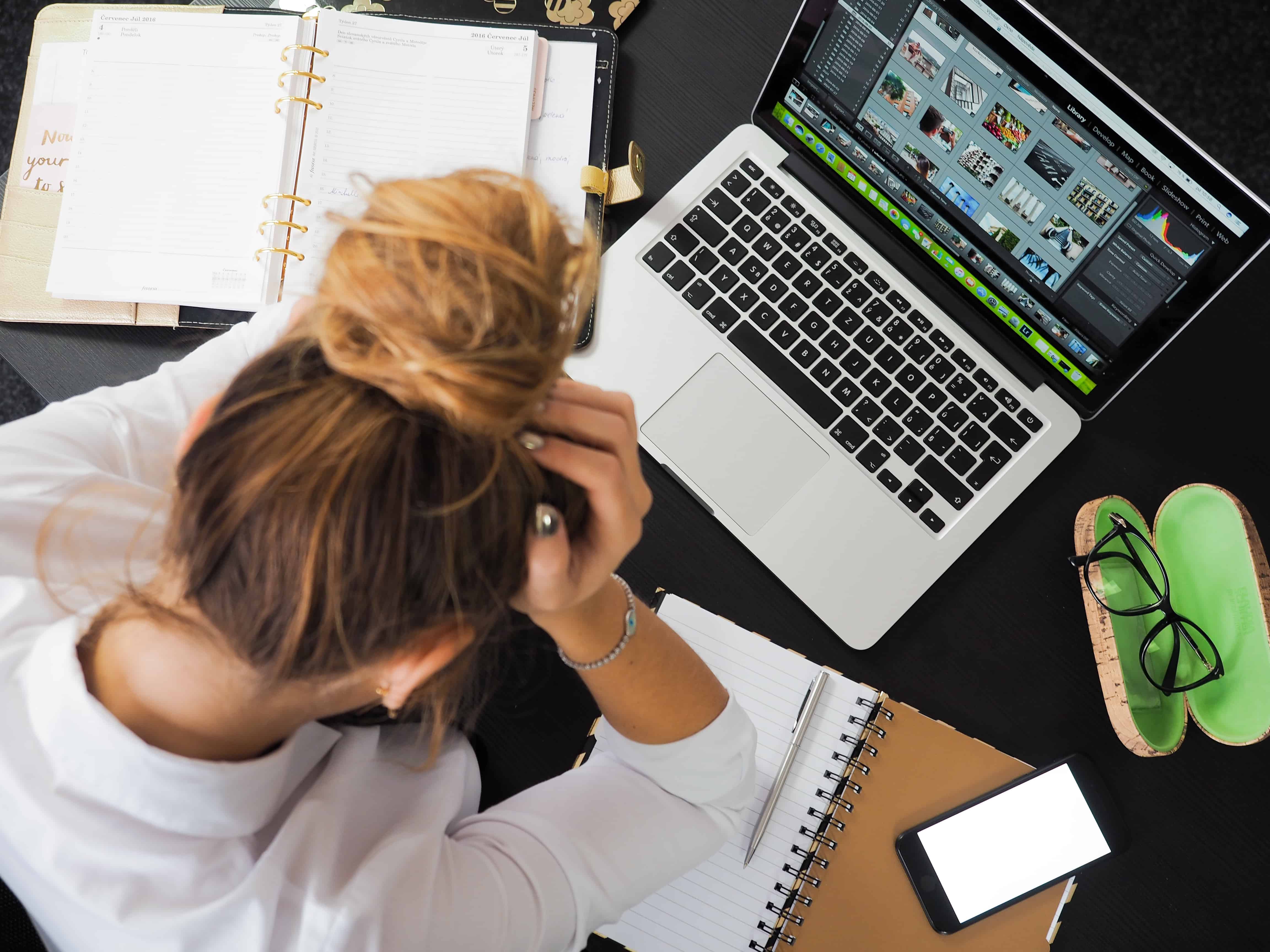 An anxiety ridden woman holds her head in worry while sitting at a desk.