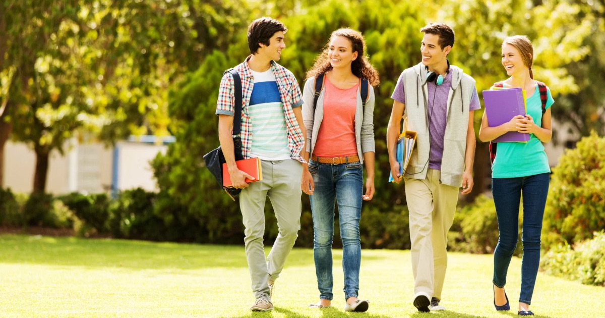 Group of college students walking together on campus with backpacks and books, smiling and talking.