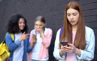 Bullied female student reading embarrassing news social networks by smartphone