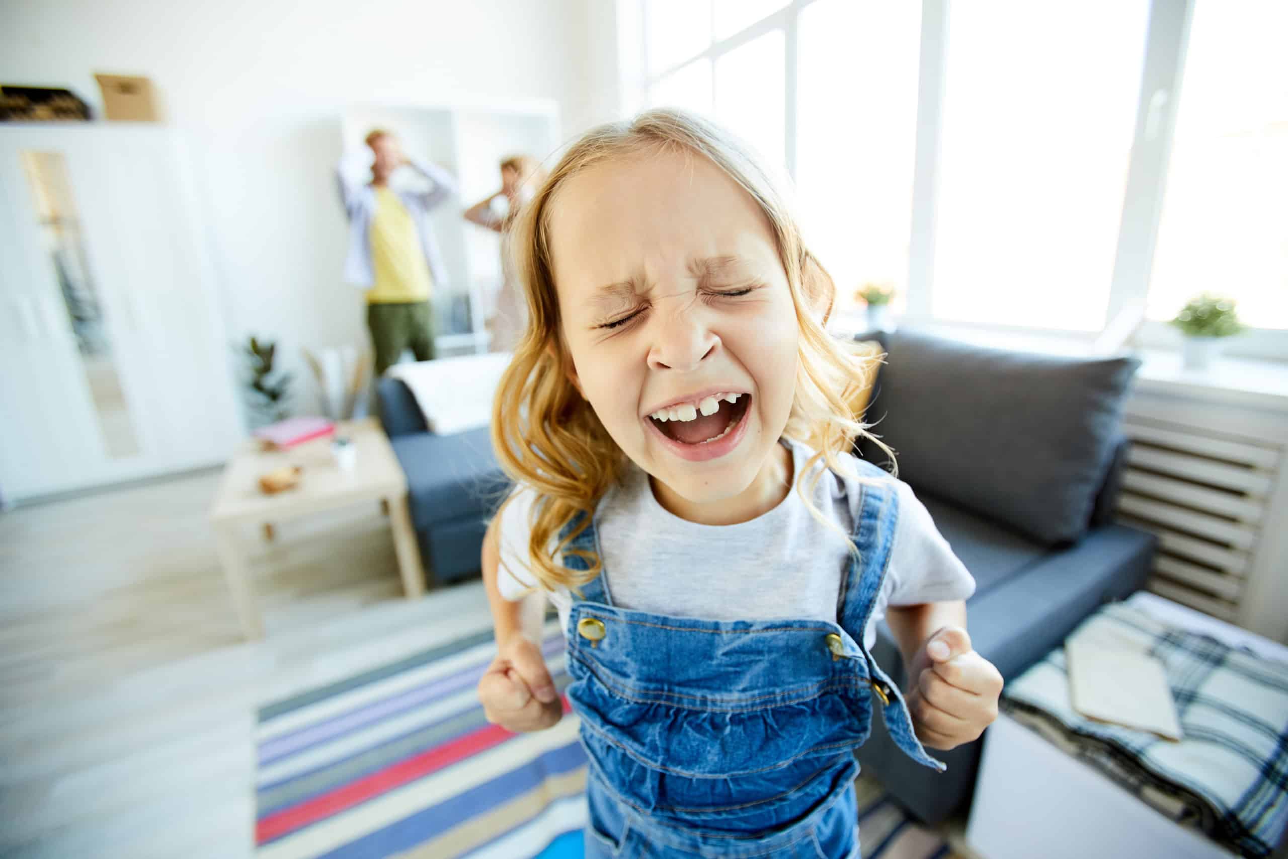 Defiant child shouting loudly while demanding something from her parents at home