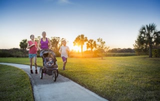 Beautiful, fit young family walking and jogging together outdoors along a paved sidewalk in a park pushing a stroller at sunset