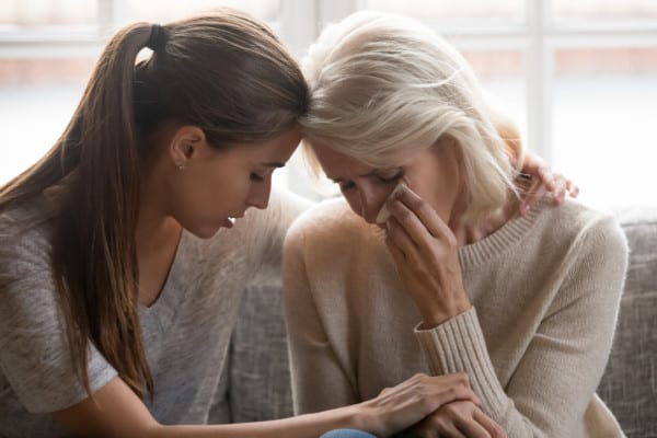 Grown up daughter soothes aged mother, holds her hand and giving her moral support