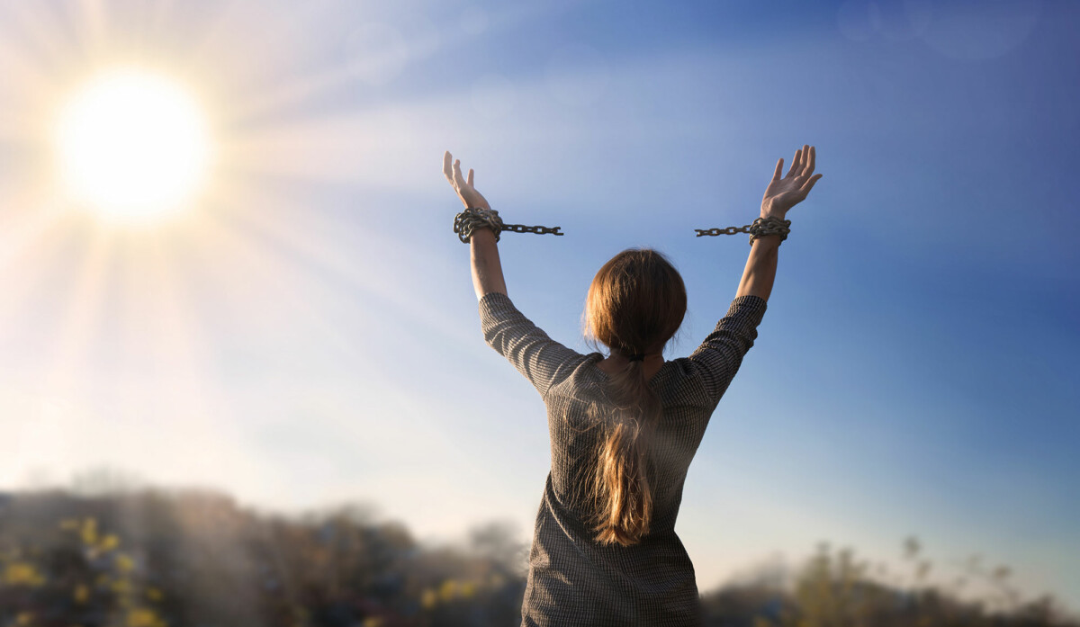 With arms uplifted to the sunlit sky a woman breaks the strong chains of bondage from her wrists.