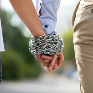 Codependent couple walk hand in hand bound together by chains.