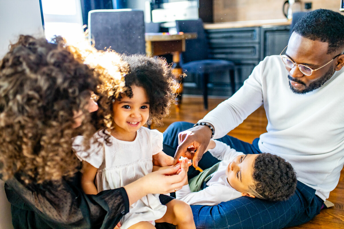 Mixed family siting on floor playing with children. Soft daylight fills the room.