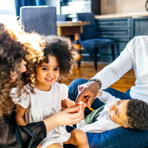 Mixed family siting on floor playing with children. Soft daylight fills the room.