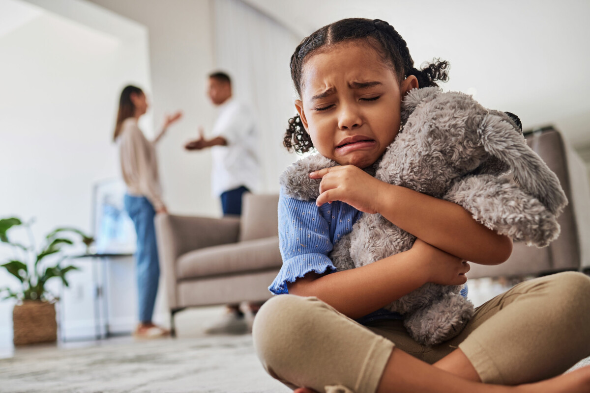 Sad, little girl hugging teddy and crying from parent argument over divorce.