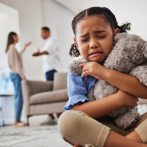 Sad, little girl hugging teddy and crying from parent argument over divorce.