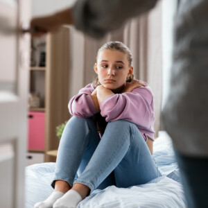 Mother opens door to reveal frustrated daughter sitting on bed at home in need of family counseling