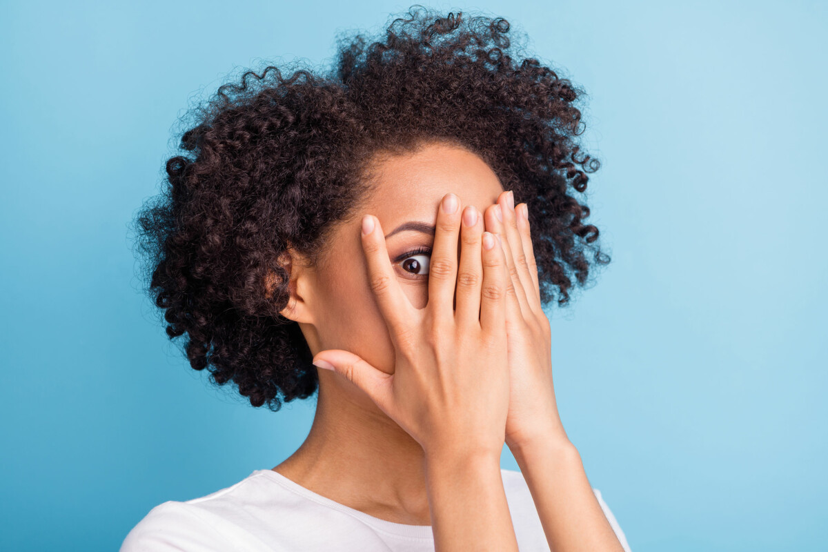 Woman peeking between fingers of hands covering her face