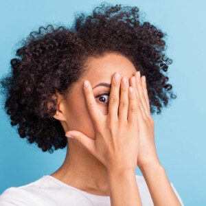 Woman peeking between fingers of hands covering her face.