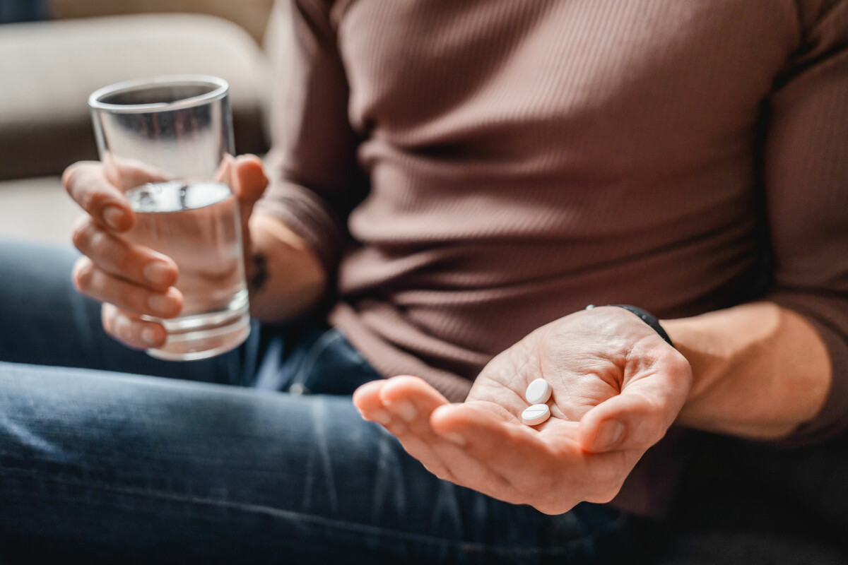 Man holding a glass of water in one hand and wellness supplements in the other