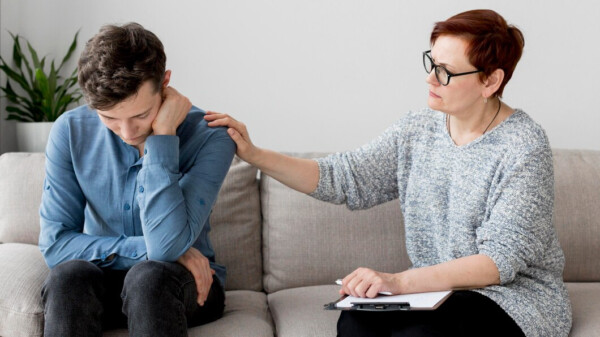 Black couple sitting on couch in an emotional embrace. Anxiety-ridden woman speaks with palms facing upwards while attentive husband provides understanding and support.