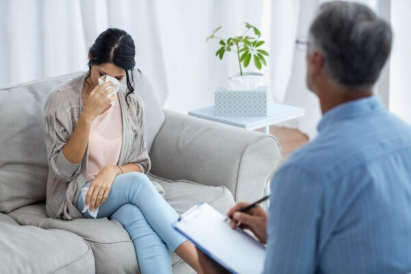 Anxiety counseling Lake Mary woman crying with tissue but getting help at Total Life Counseling Anxious mother consumed by worry holds baby while staring blindly into the distance. Supportive husband looks upon his wife with concern.