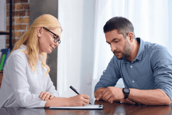 Man pointing by finger on clipboard of female psychiatrist while she taking notes