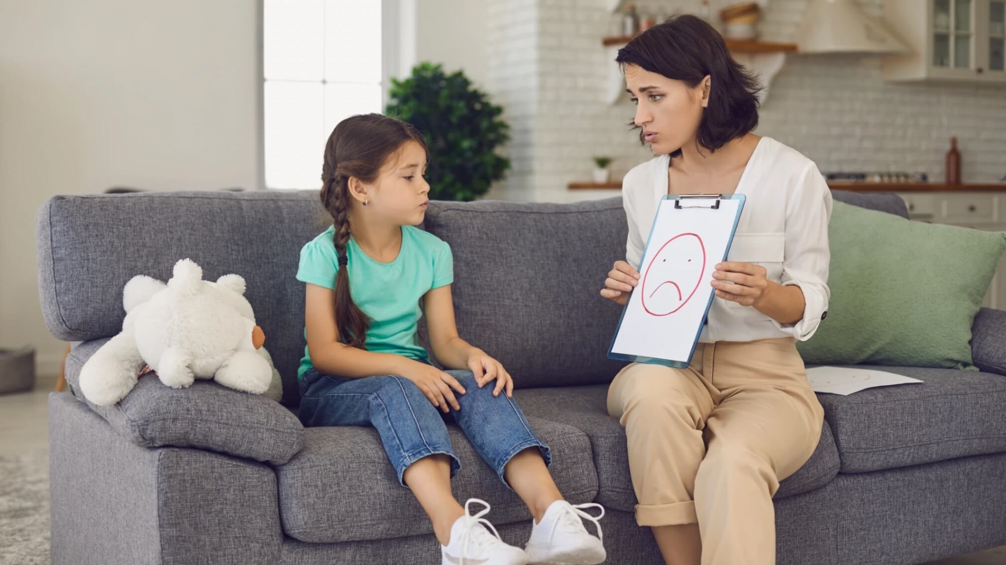 Child in therapy session with psychologist showing sad face drawing.
