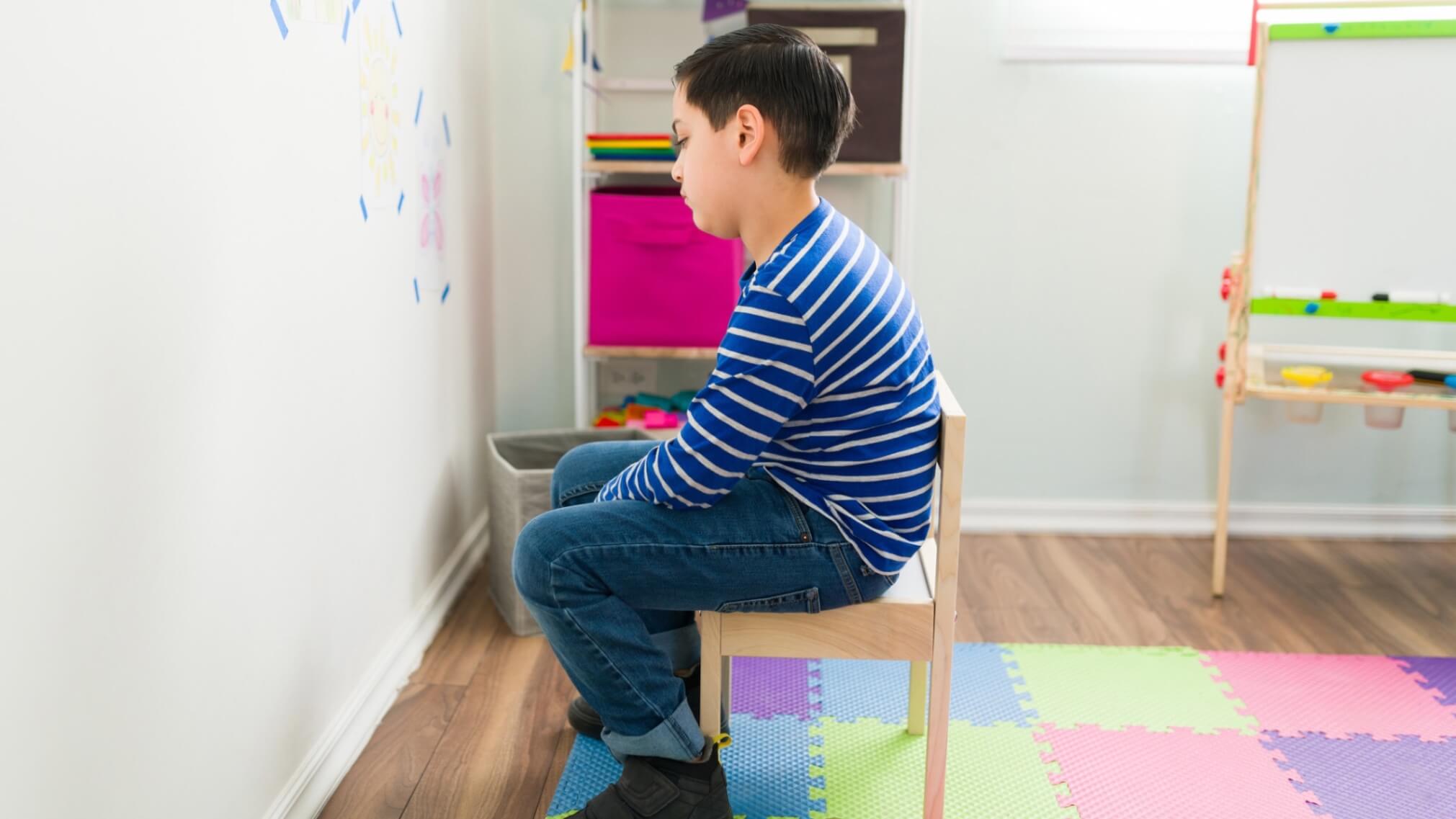 Child sitting alone in classroom looking upset.