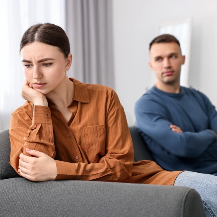 Couple sitting apart on couch, looking upset.