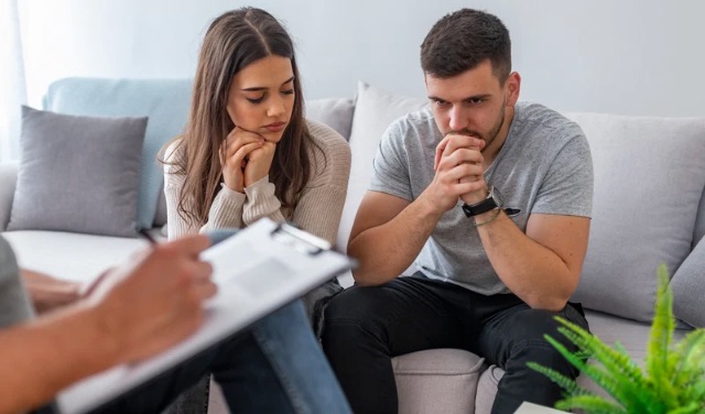 Couple sitting with therapist, appearing thoughtful and concerned during counseling session.