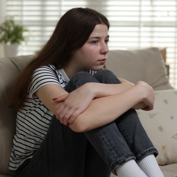 Teen girl sitting on a couch with arms around knees, appearing depressed. Teen girl sitting on a couch with arms around knees, appearing depressed.
