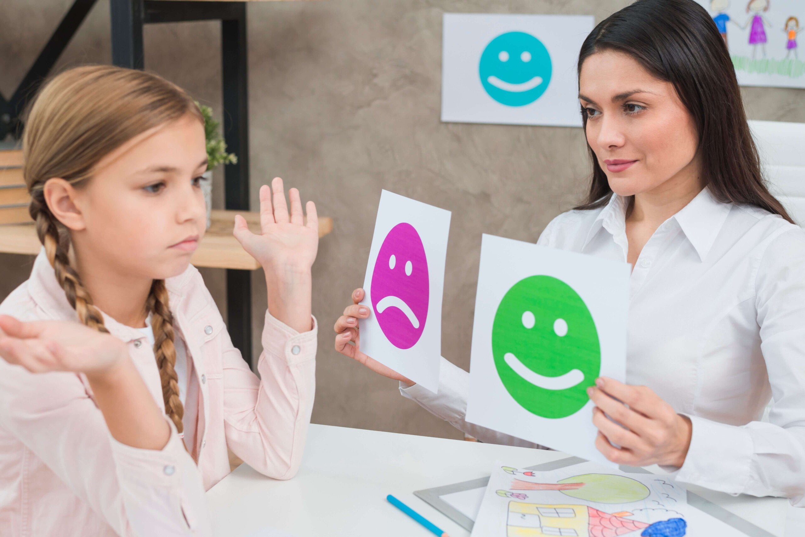 A psychologist showing happy and sad emotion faces cards to the girl A psychologist showing happy and sad emotion faces cards to the girl