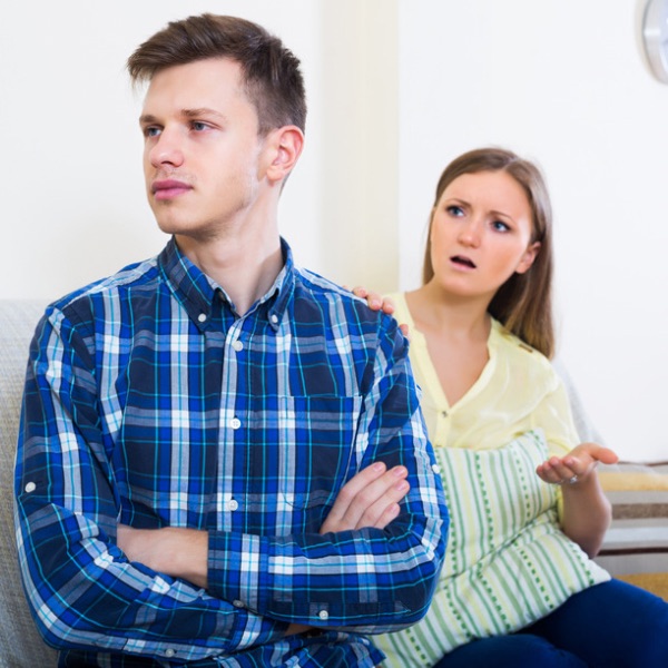 Couple arguing on a couch, with the man looking away and the woman appearing upset and gesturing while talking