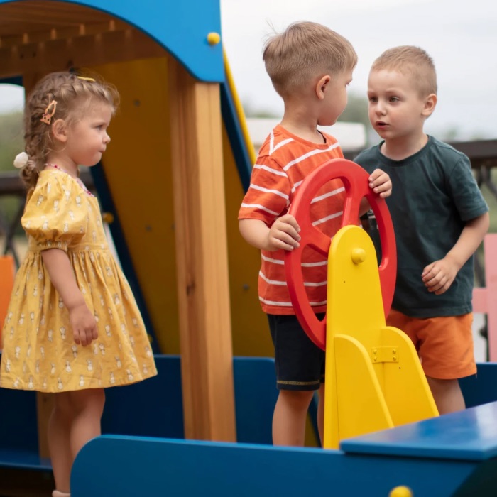 Three young children on a playground, appearing to have a disagreement or tense interaction near a play structure.