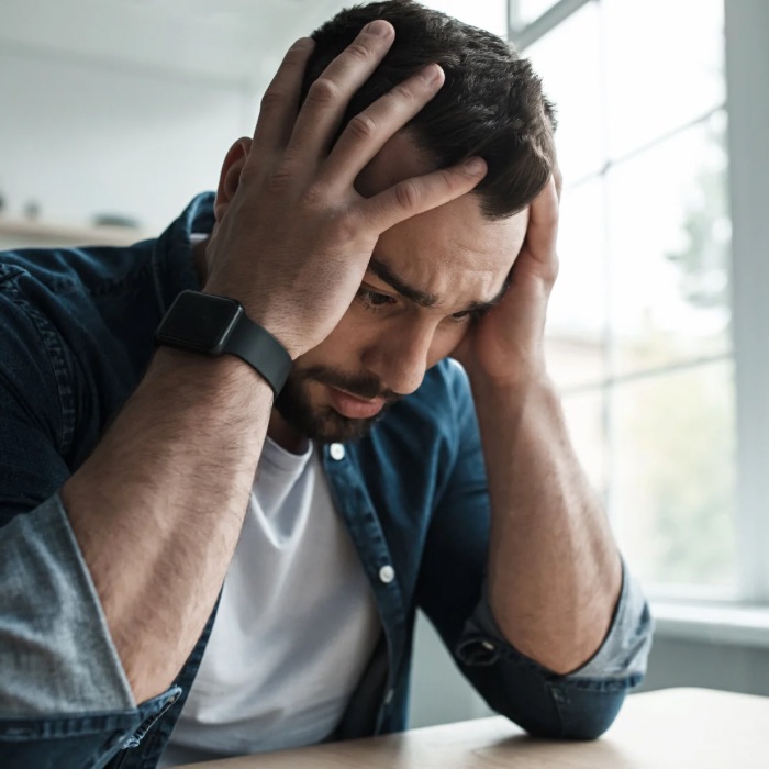 Stressed young man sitting at a table, holding his head in his hands, looking overwhelmed.