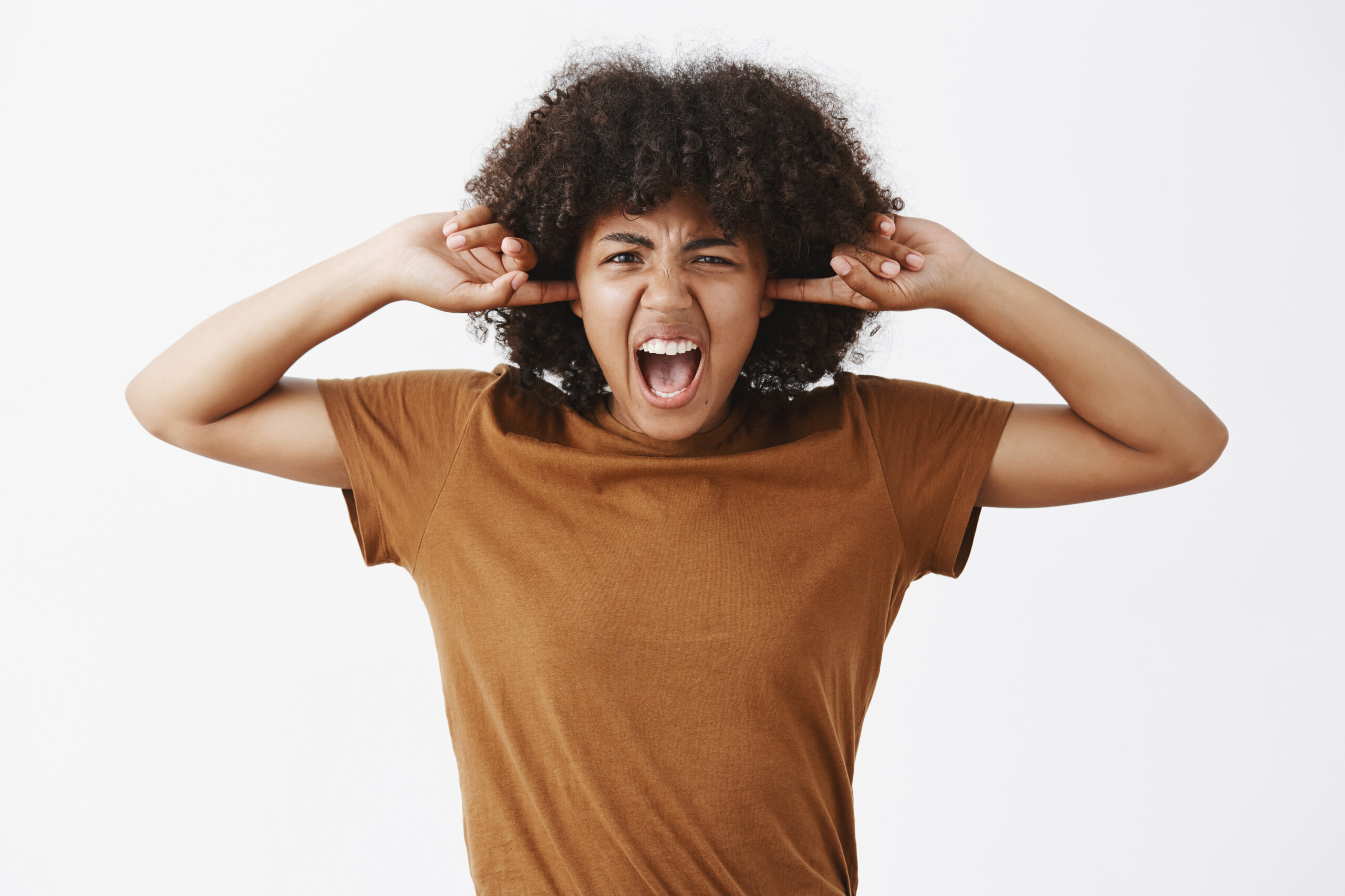 Waist-up shot of fed up pissed off stylish young woman with curly hairstyle in brown t-shirt covering ears with fingers and yelling frowning from annoyance and dislike demanding brother turn music off - Total Life Counseling for Children, Teens, Adolescents and Adults in Orlando Winter Park Clermont Lake Mary and Central Florida Anti-Bullying School Program