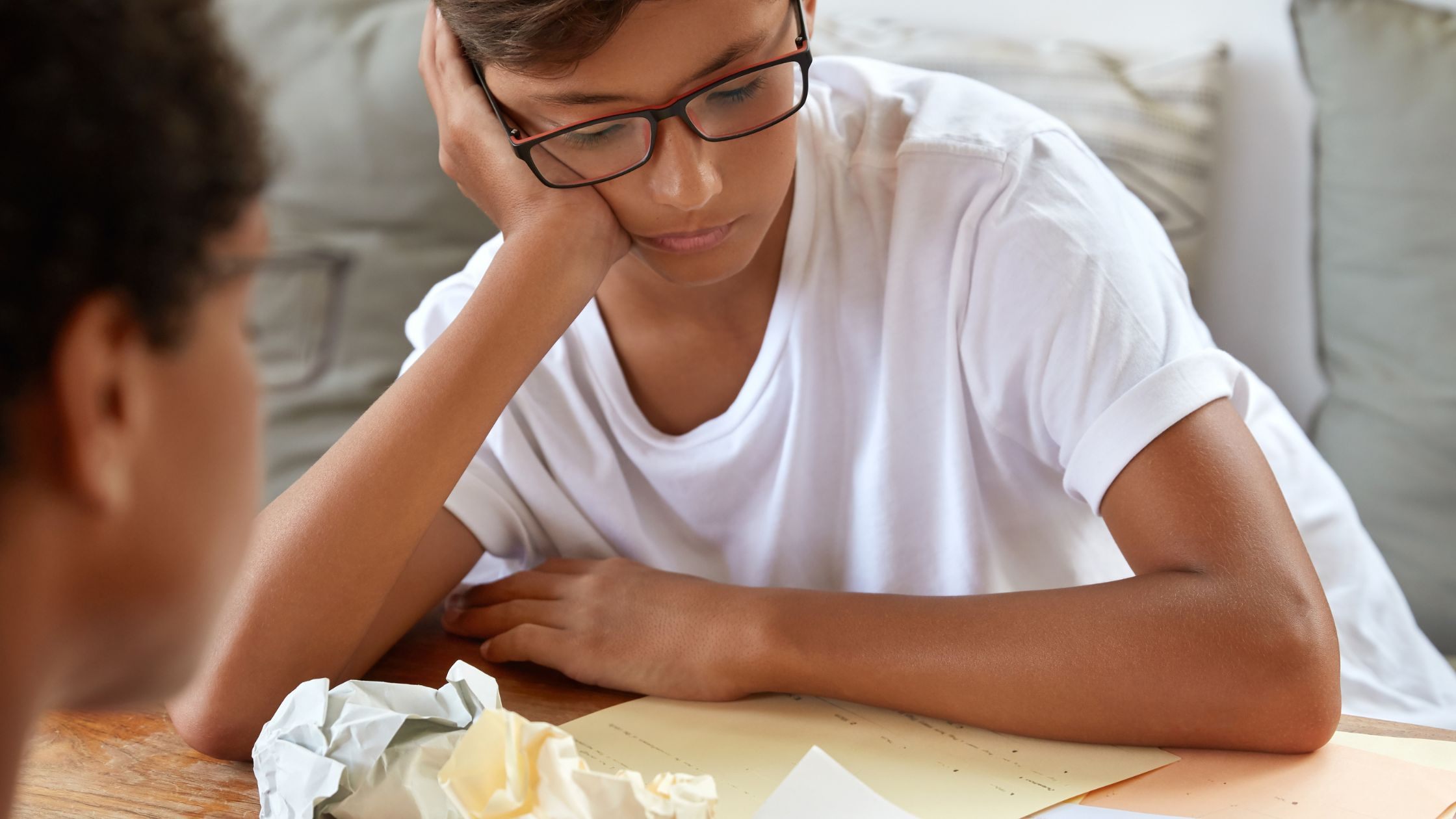 Boy struggling with homework while receiving help at a table