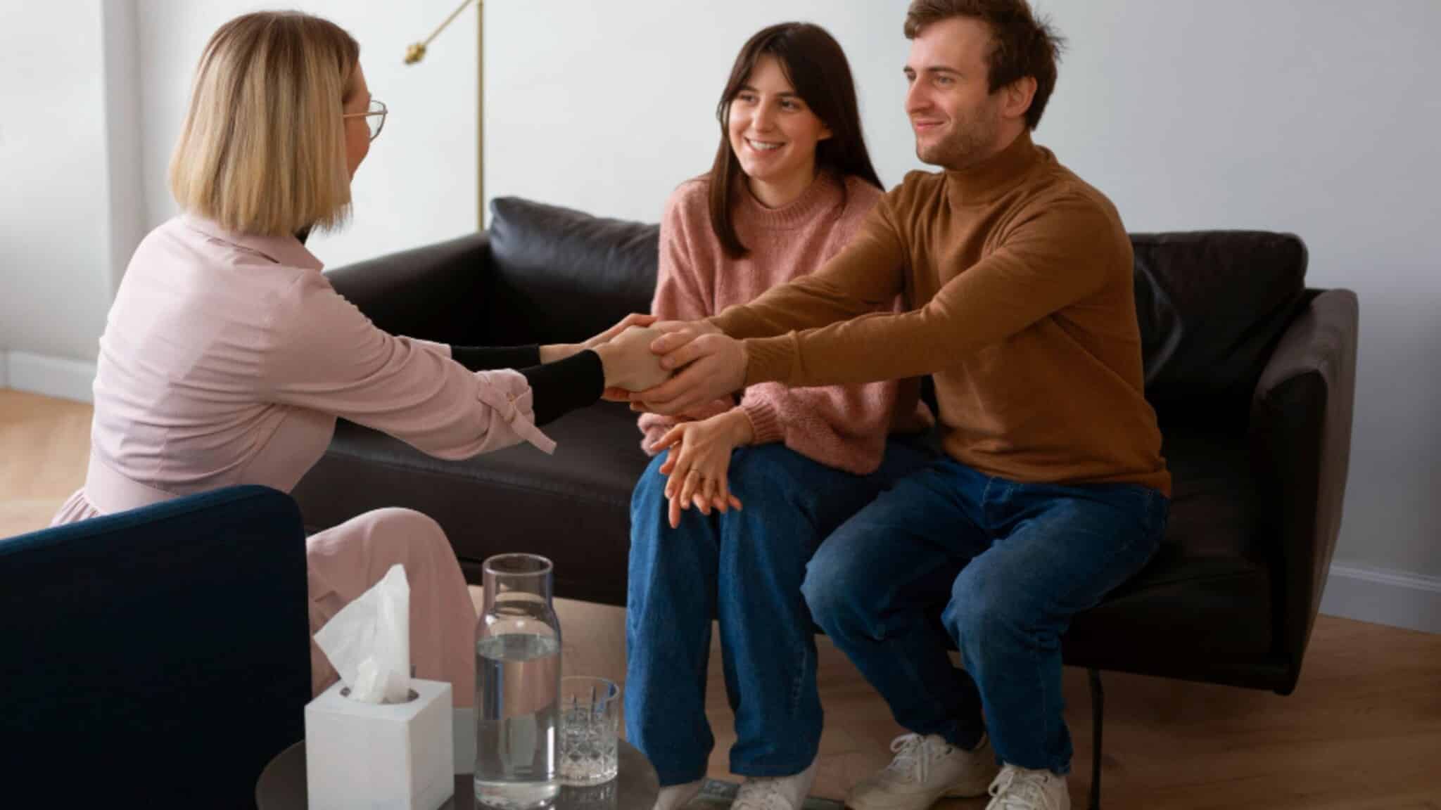 image – 2026-06-17T160442857 - Total Life Counseling for Children, Teens, Adolescents and Adults in Orlando Winter Park Clermont Lake Mary and Central Florida Therapist sits with a couple on a couch, all smiling as they hold hands in a supportive counseling session.